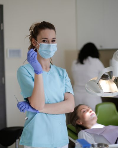 Dentist with tweezers and mirror standing near patient in clinic